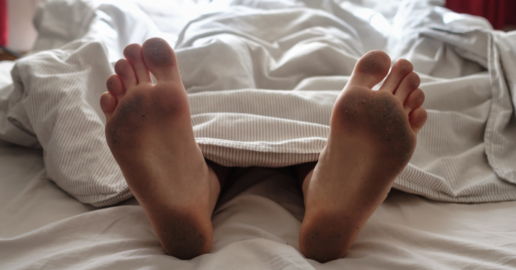Dreckige Füße gucken aus dem Bett heraus