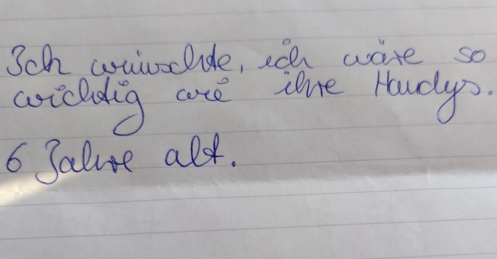 Ein liniertes Blatt Papier, auf dem mit blauem Kugelschreiber steht: „Ich wünschte, ich wäre so wichtig wie ihre Handys.“ 6 Jahre alt