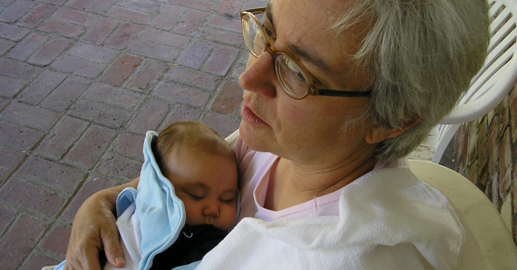 Eine Frau mit grauen Haaren und Brille hält ein Baby nah an sich.