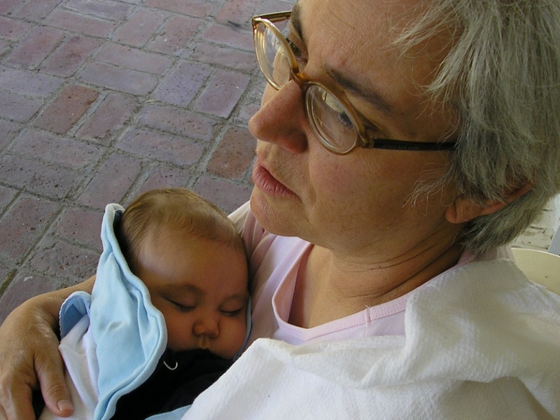 Eine Frau mit grauen Haaren und Brille hält ein Baby nah an isich