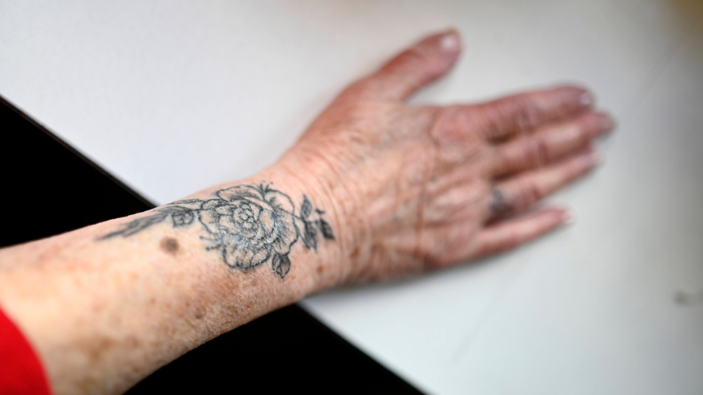Der Arm einer älteren Person mit Blumen-Tattoo darauf.