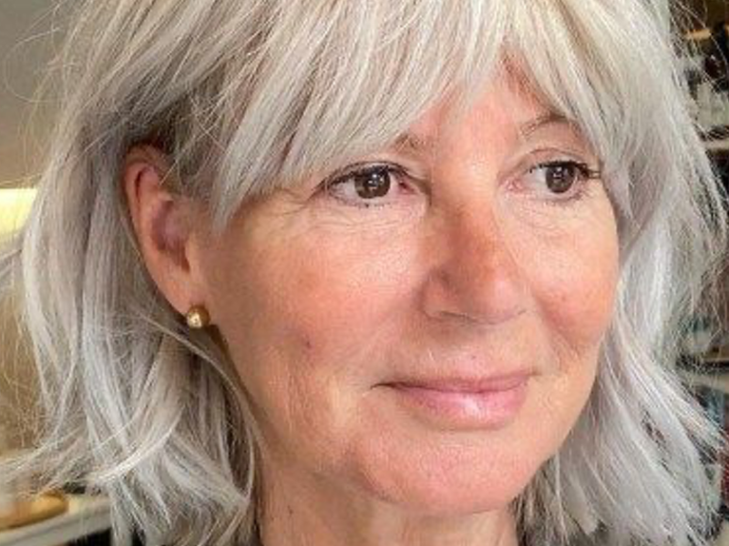 Eine Frau mit einer mittellangen Frisur und grauen Haaren schaut an der Kamera vorbei