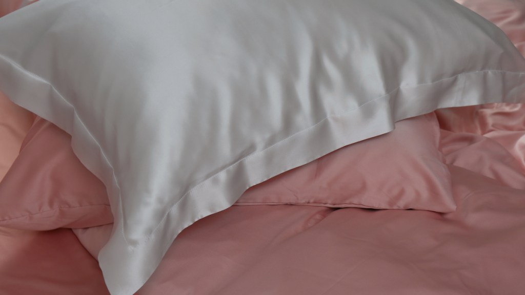 Ein weißer Kissenbezug aus Seide liegt auf einem rosa-bezogenen Bett.