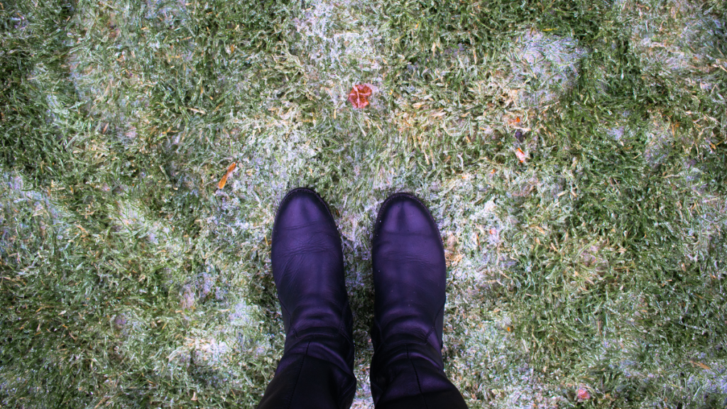 Eine Person in Stiefeln steht auf leicht verschneitem Rasen.