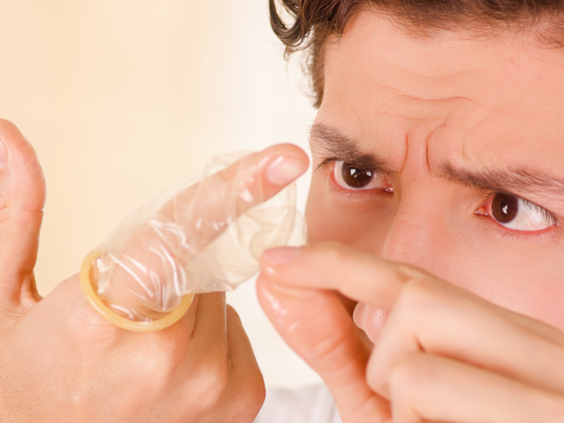 Ein Mann untersucht ein Kondom, das er über den Zeigefinger gezogen hat.