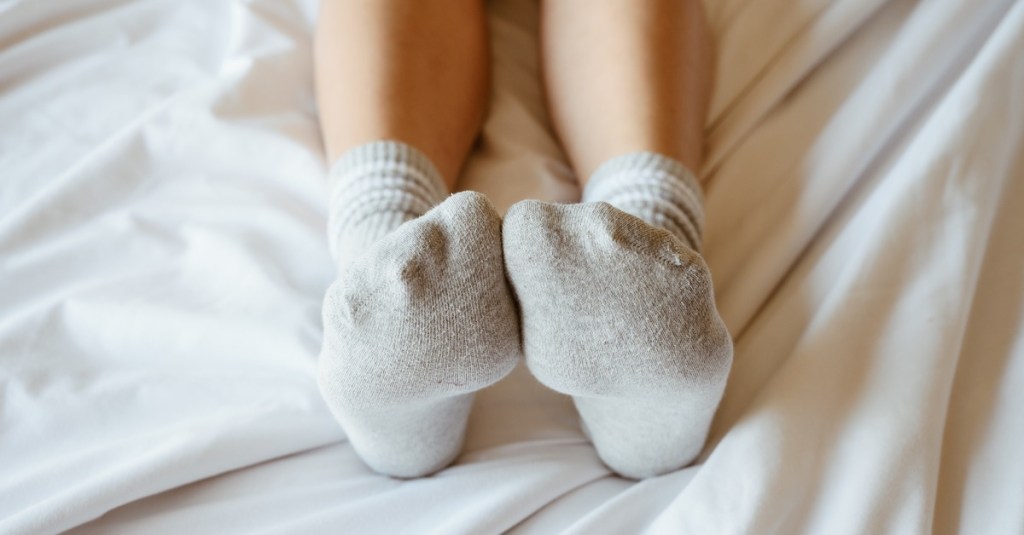 Frau liegt im Bett und hat Socken an.