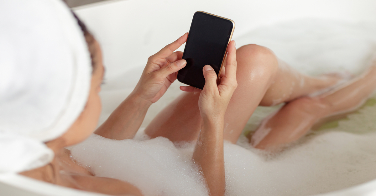 Frau mit Smartphone in der Badewanne.