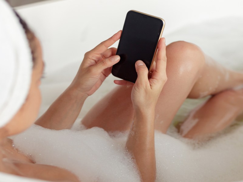 Frau mit Smartphone in der Badewanne.