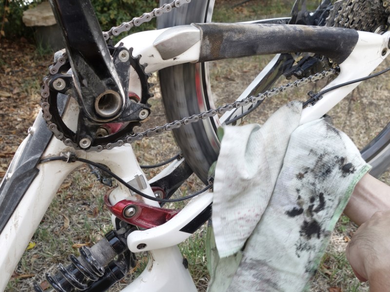 Ein Lappen der voller Dreck und Schmiere ist, im Hintergrund ein schmutziges, weißes Fahrrad, das auf dem Kopf steht.