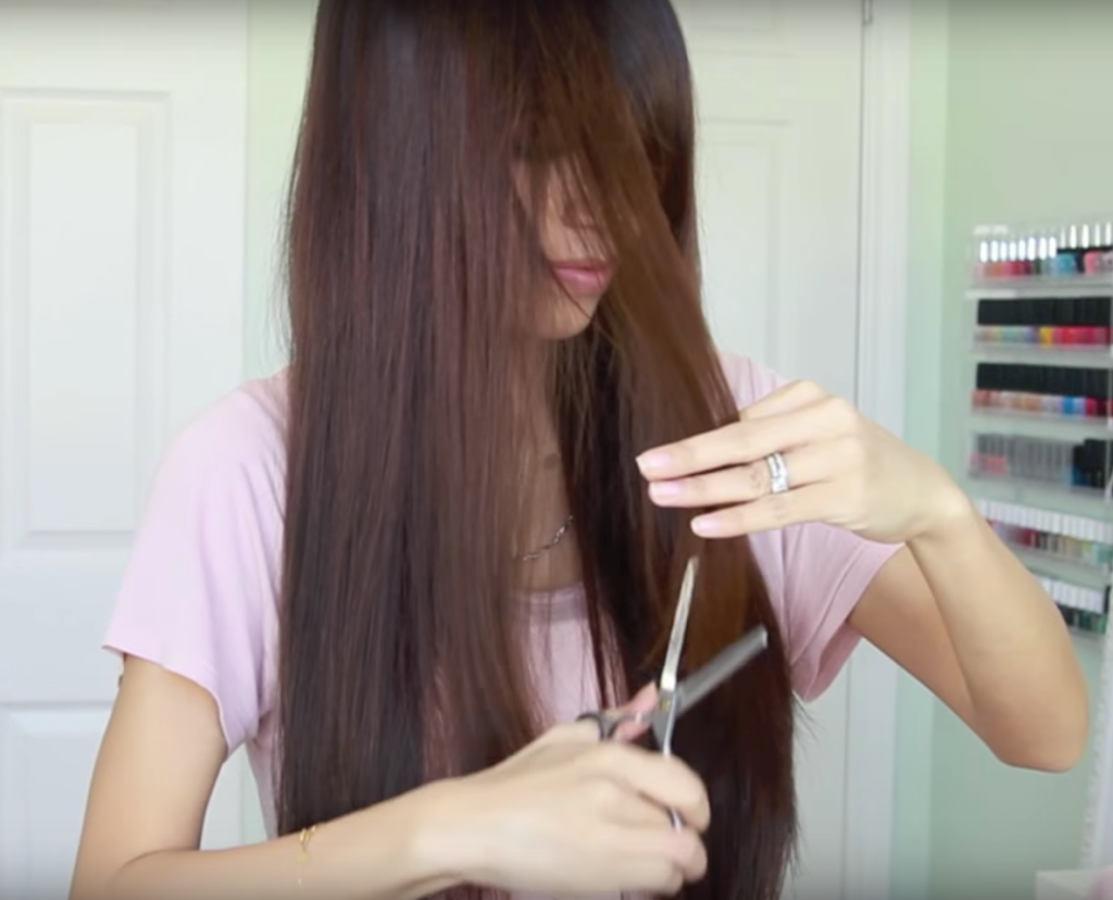 Eine Frau schneidet ihre Haare mit einer Modellierschere.