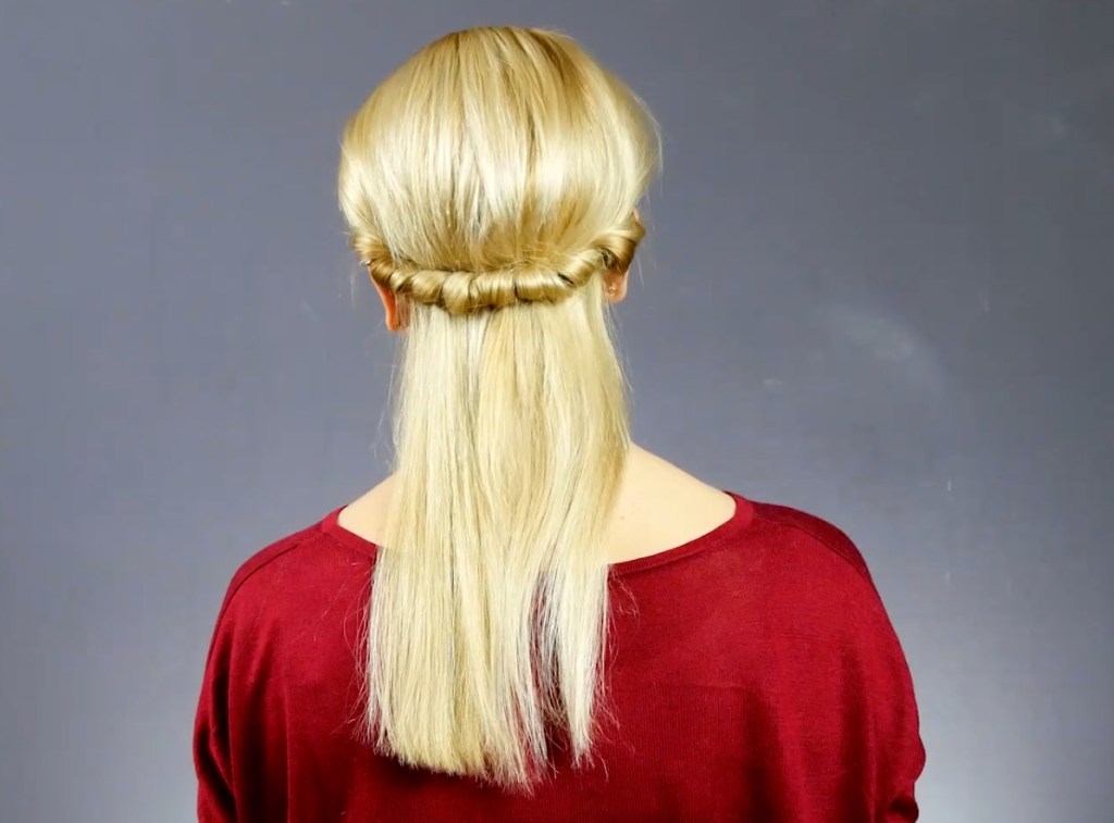 Von hinten fotografiert: Eine blonde Frau hat offene Haare, jedoch einen Teil der Strähnen zu einem Kranz im Nacken geflochten.