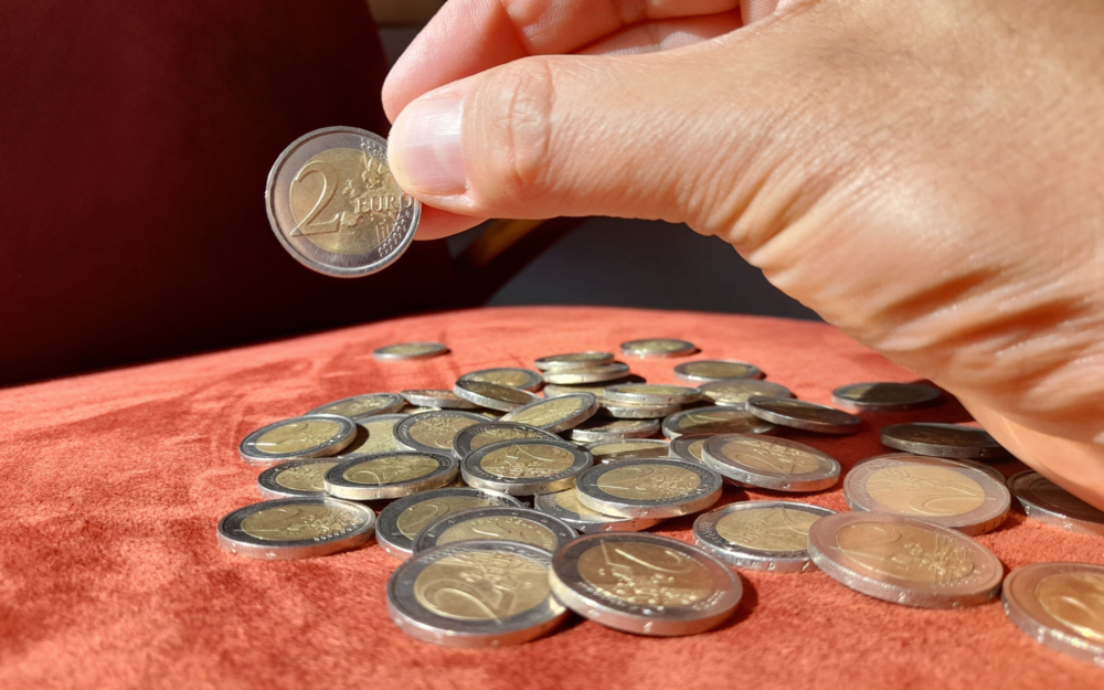 2-Euro-MÃ¼nzen auf einem Tisch. Jemand hÃ¤lt eine MÃ¼nze in der Hand.