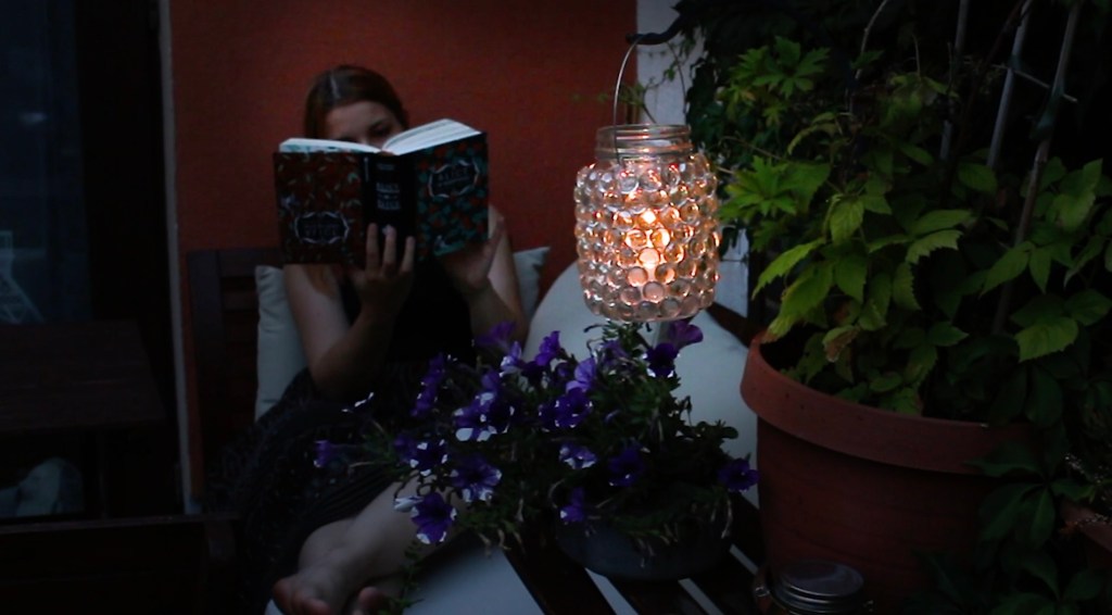 Eine Frau liest bei Kerzenschein im Garten.