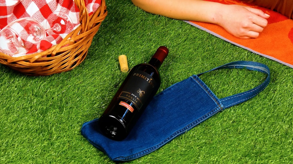 Die Jeanstasche liegt auf einem grÃ¼nen Rasen und darauf eine Rotweinflasche.