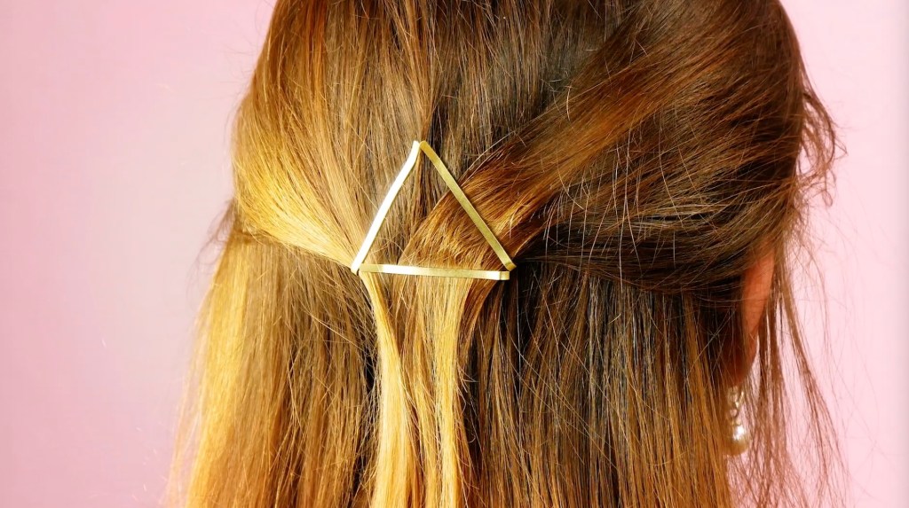 Eine Raute aus zwei goldenen Haarklammern in braunem Haar.