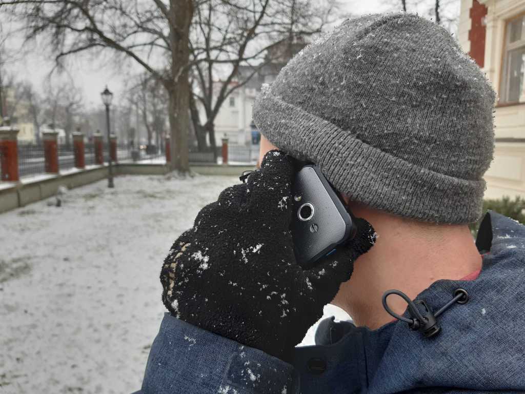 Ein Mann in Mütze und Handschuhen hält sein Smartphone ans Ohr.