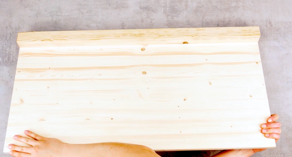 Eine helle Holzplatte wird in die Kamera gehalten.