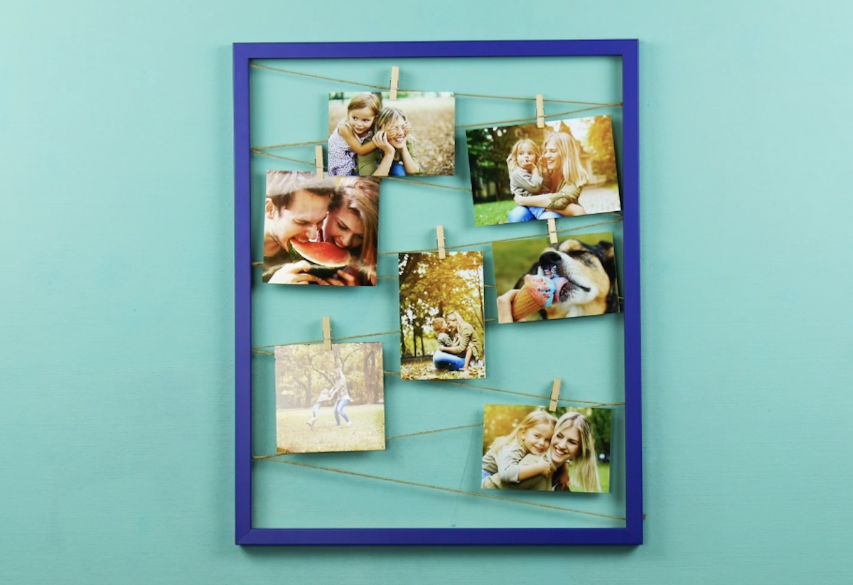 Ein blauer Bilderrahmen mit FÃ¤den, an denen mit WÃ¤scheklammern Fotos befestigt sind.