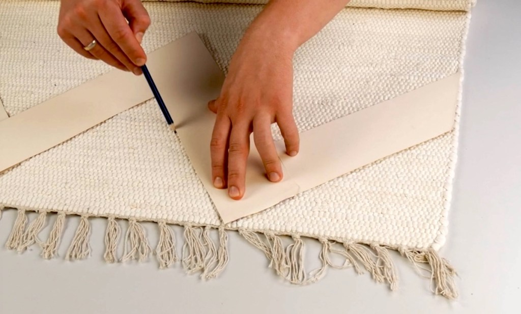 Mithilfe einer Pappschablone wird ein Muster in einen Teppich gezeichnet.