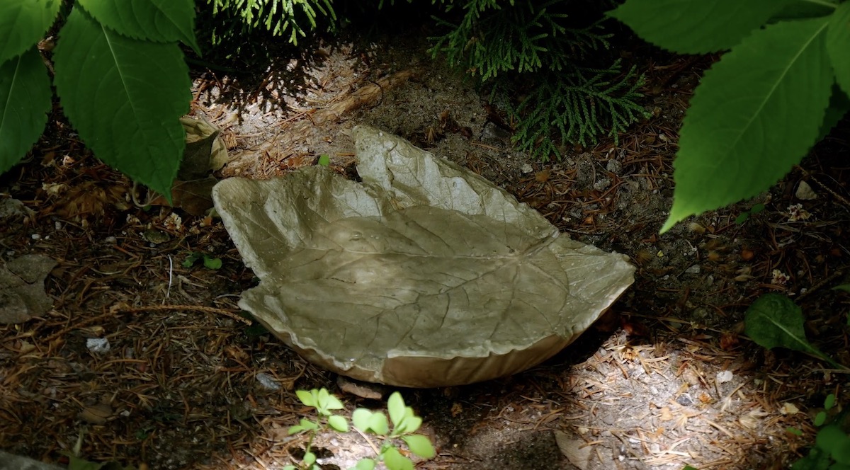 Eine Beton-Schale in Blattform liegt in einem Blumenbeet.