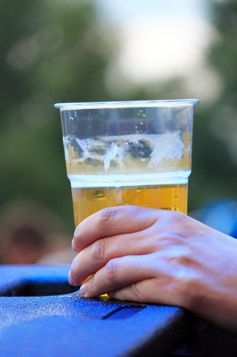 Hand hält Plastikbecher mit Bier. Warum es anders schmeckt als aus dem Glas, ist eine oft gestellte Alltagsfrage.