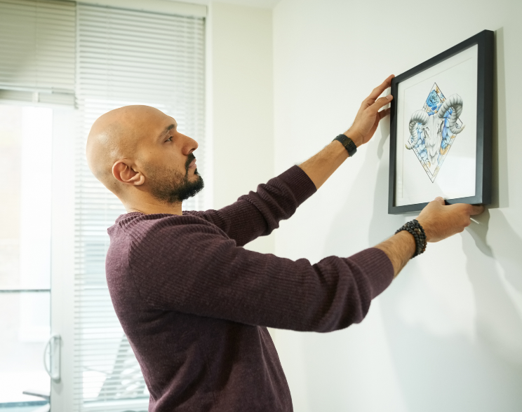 Ein Mann richtet einen Bilderrahmen an der Wand aus.