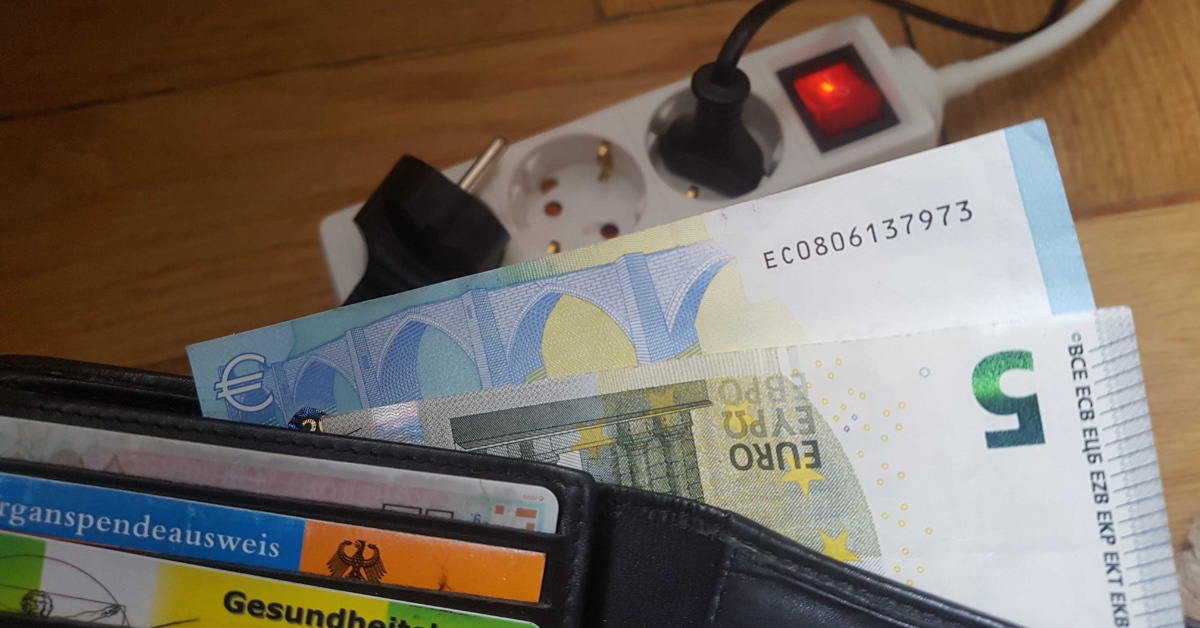 Ein Foto von Geldscheinen in einem Portemonnaie neben einer Steckdose.