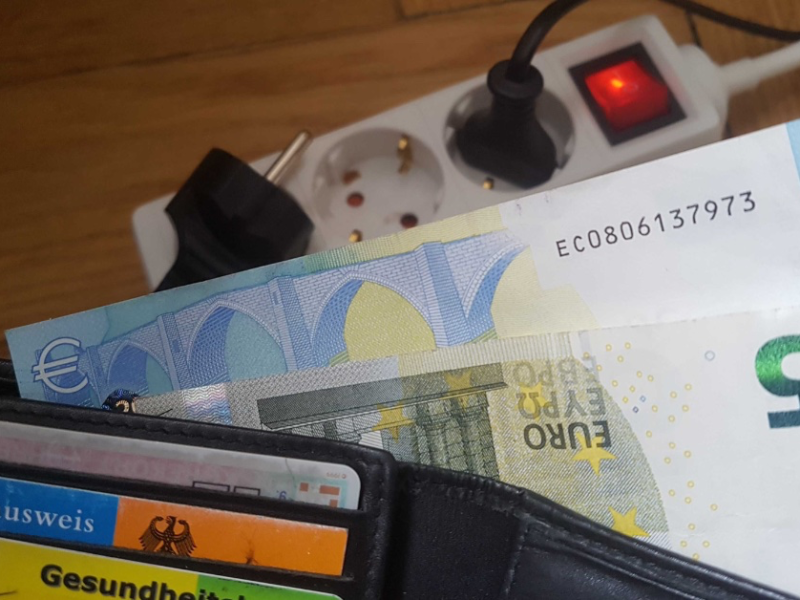 Ein Foto von Geldscheinen in einem Portemonnaie neben einer Steckdose.