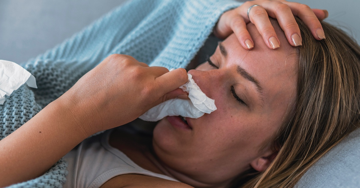 Frau liegt mit Fieber im Bett. Wadenwickel bei Fieber sind ein altes Hausmittel gegen Erkältung.