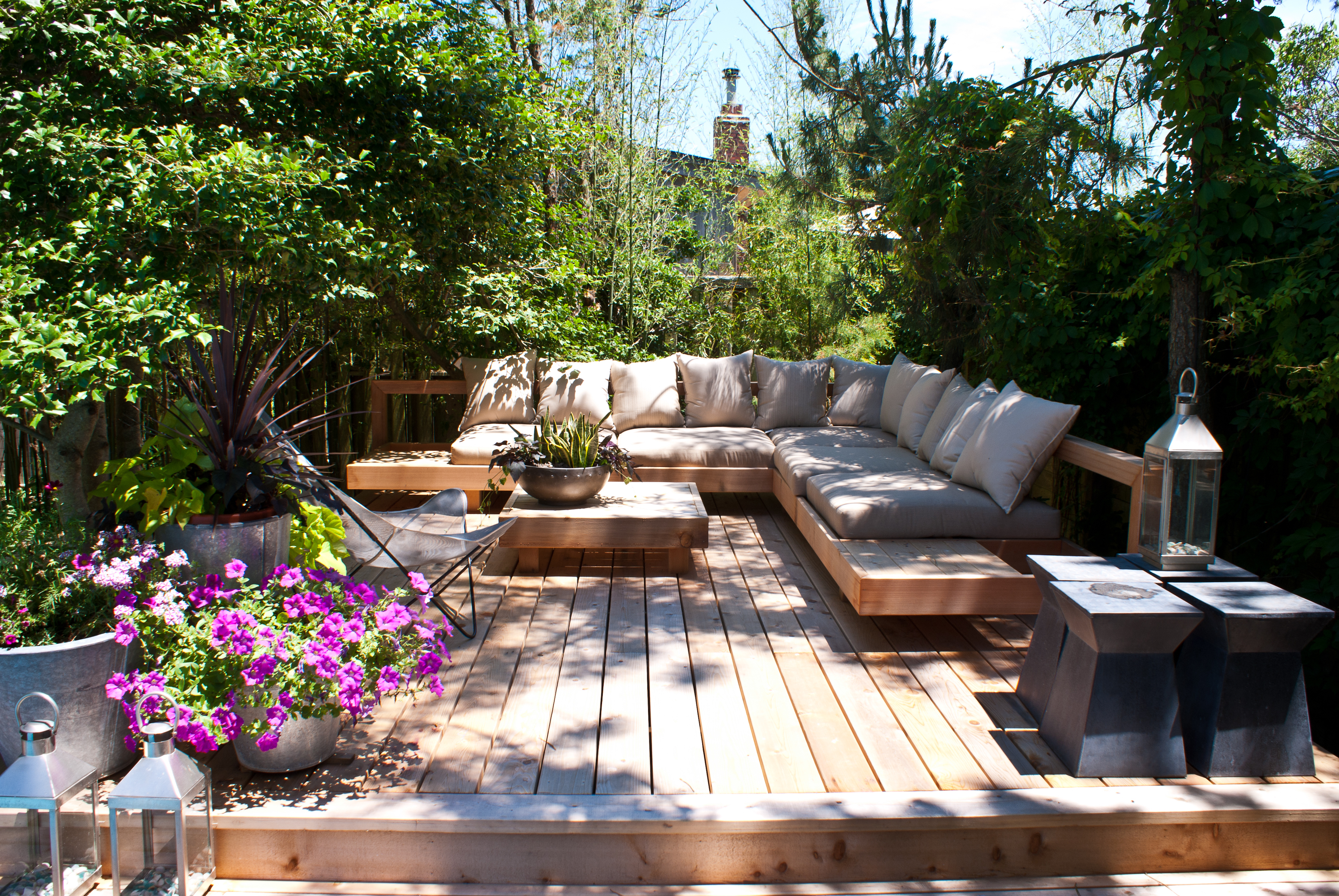 Eine gemÃ¼tliche Terrasse mit Holzbohlen und einem Sofa. Rundherum ein Sichtschutz aus Pflanzen.