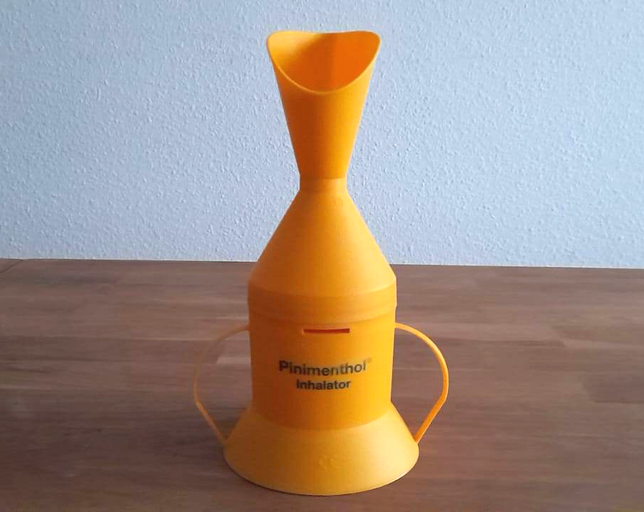 Ein orangefarbener Inhalator aus Kunststoff steht auf einem Tisch. RegelmÃ¤ÃŸiges Inhalieren bei Schnupfen kann die Symptome schneller lindern.