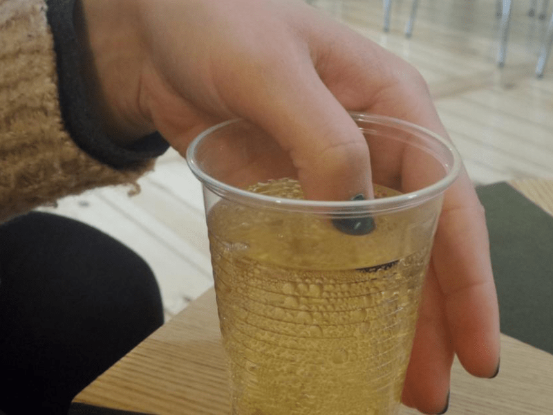Eine Frau hält einen lackierten Fingernagel in ein alkoholisches Getränk. Kann man mithilfe eines Nagellacks K.-o.-Tropfen erkennen?
