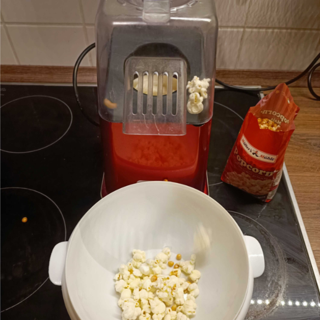 Popcorn ploppt aus einer Popcorn-Maschine in eine weiÃŸe SchÃ¼ssel.