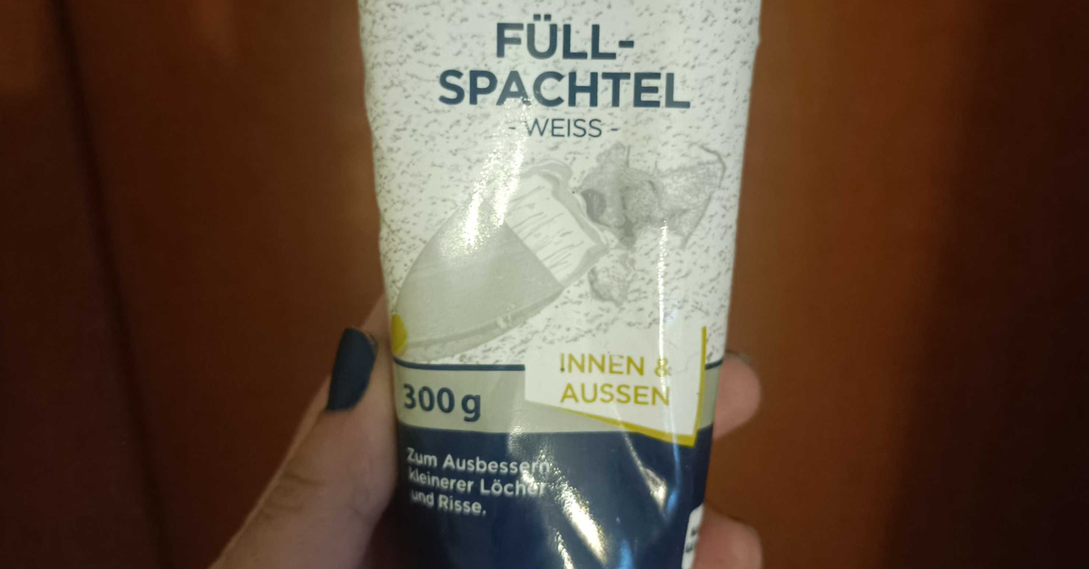 Eine Hand hält eine Tube Spachtelmasse ins Bild.