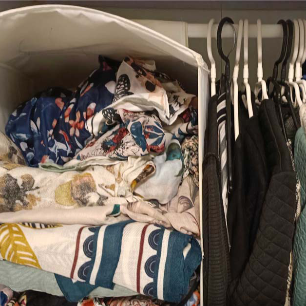 Schals tÃ¼rmen sich unordentlich in einem Fach im Kleiderschrank neben Kleidung auf BÃ¼geln. 