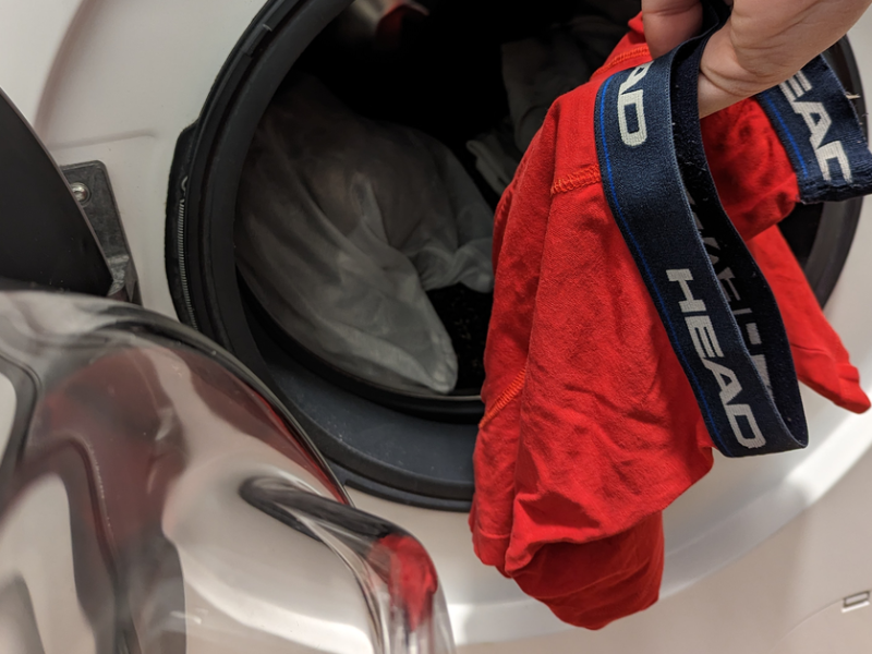 Eine rote Boxershorts wird in eine Waschmaschine gesteckt.