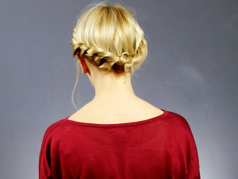 Von hinten fotografiert: Eine blonde Frau mit einem geflochtenen Haarkranz im Nacken.
