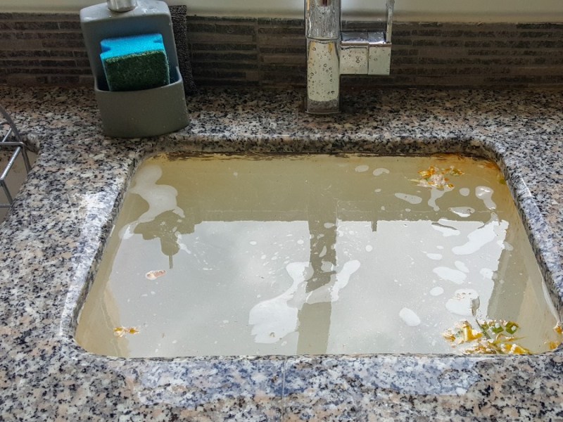 Ein schmutziges Waschbecken in einer Küche wird mit Wasser befüllt.