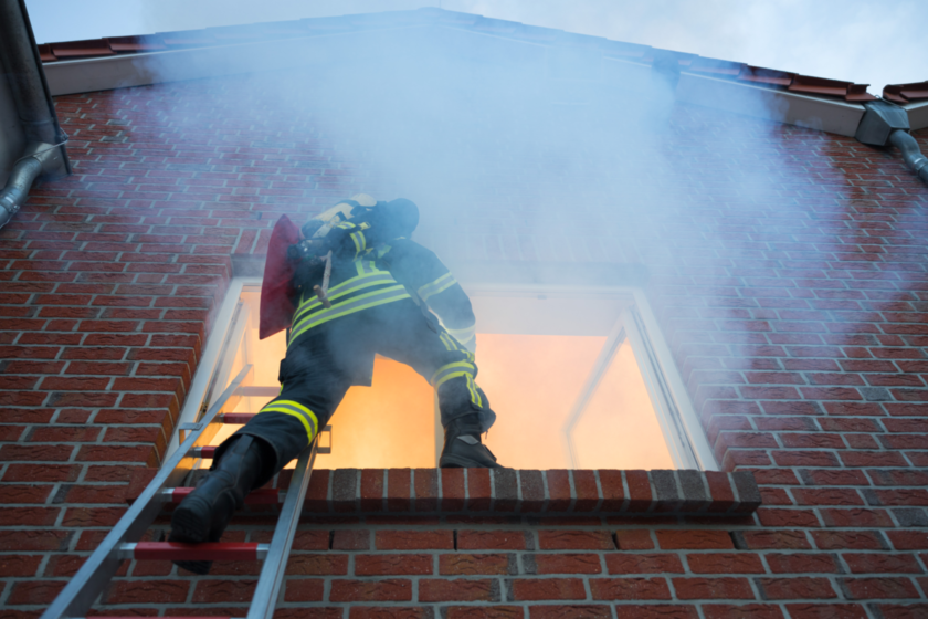 brandschutz Ein Feuerwehrmann klettert über eine Leiter in ein brennendes Haus.