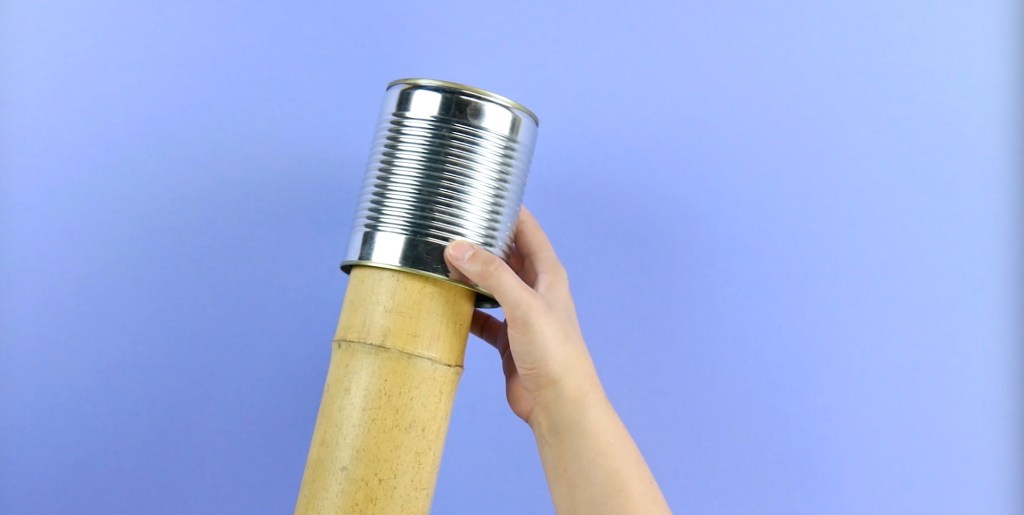 Ein Bambusrohr wird in eine Blechdose geschoben.