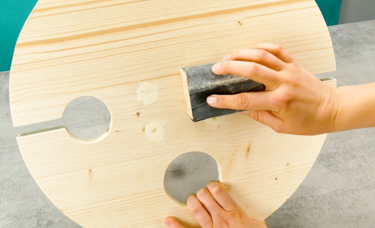 Jemand schleift die Fläche des Tisches mit Schleichpapier und einem Schleifblock ab.