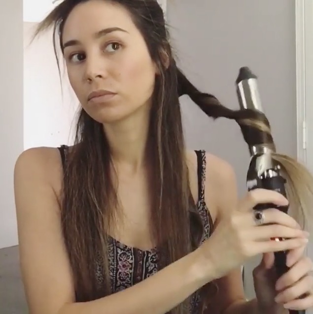 Eine Frau stylt ihre langen, braunen Haare mit einem Lockenstab.