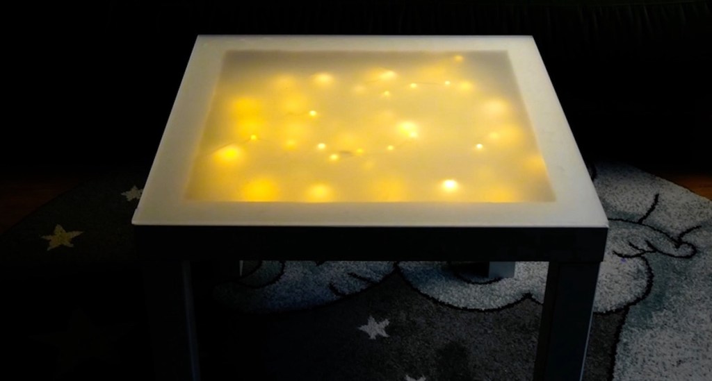 Ein mit Plexiglas als Platte leuchtender IKEA-Tisch.