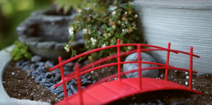 Eine rote Modell-Brücke in einem Mini-Zengarten.