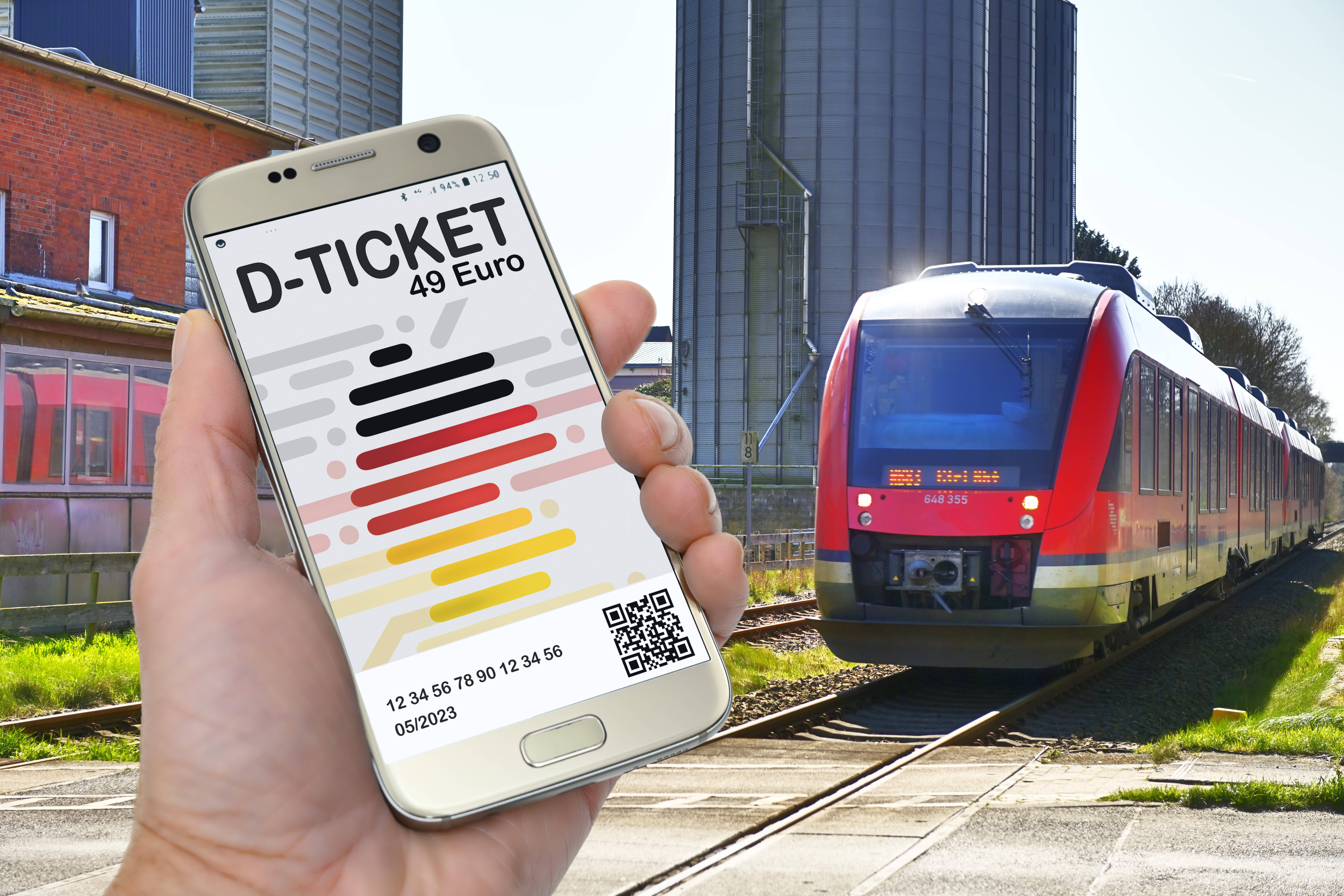 Das Deutschlandticket wird auf einem Handy angezeigt. Im Hintergrund ist ein Regionalzug zu sehen.