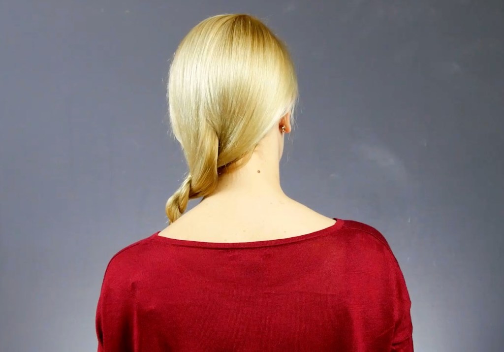Von hinten fotografiert: Eine blonde Frau hat einen geflochtenen Zopf über ihre linke Schulter gelegt.