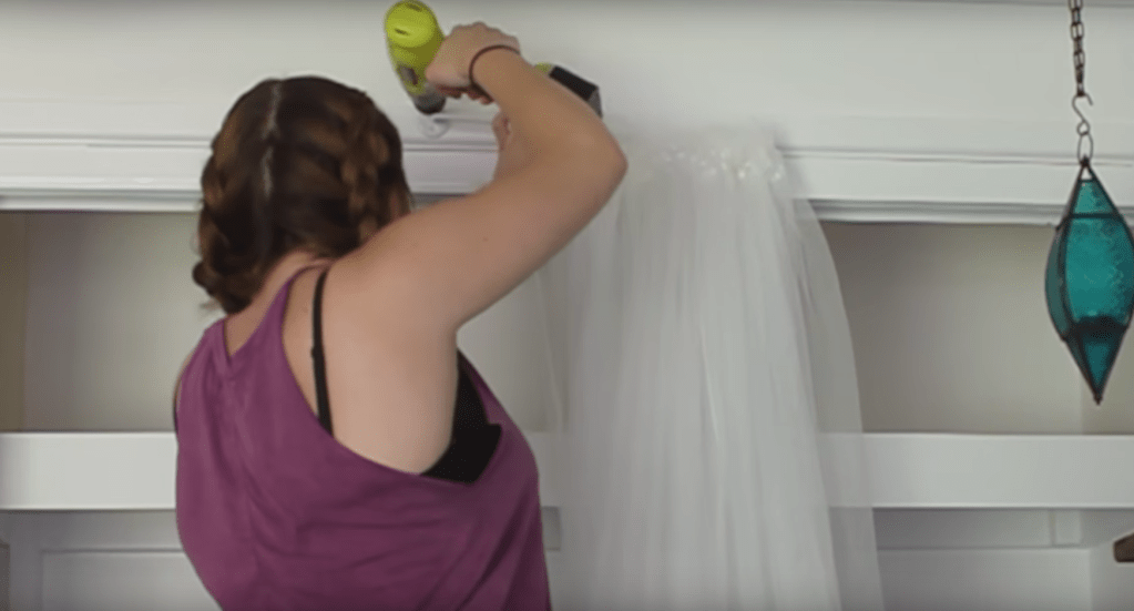 Eine Frau befestigt eine weiße Gardine an einem Wandschrank.