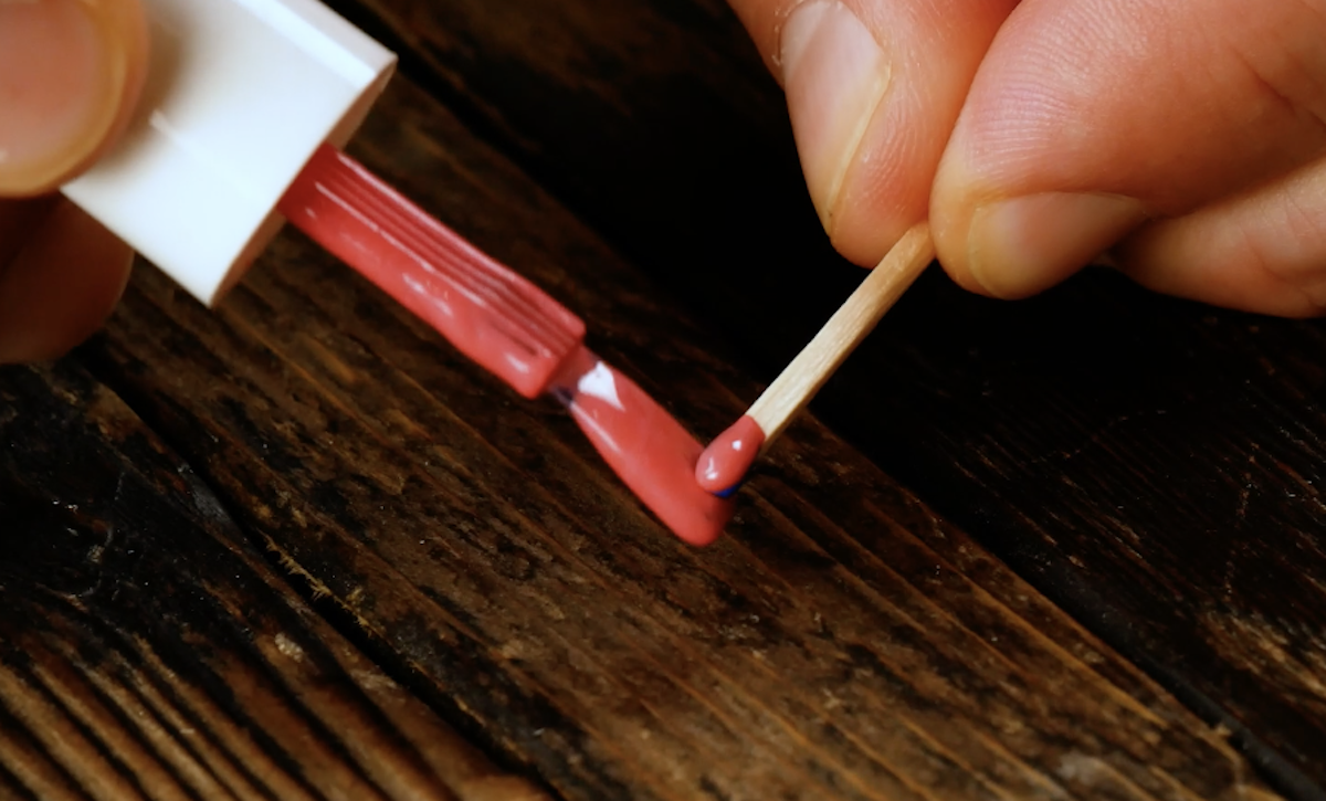 Die Spitze eines Streichholzes wird mit rotem Nagellack bepinselt.
