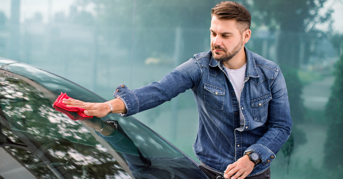 Ein Mann in Jeanshemd wischt mit einem roten Lappen Ã¼ber die Windschutzscheibe eines Autos.