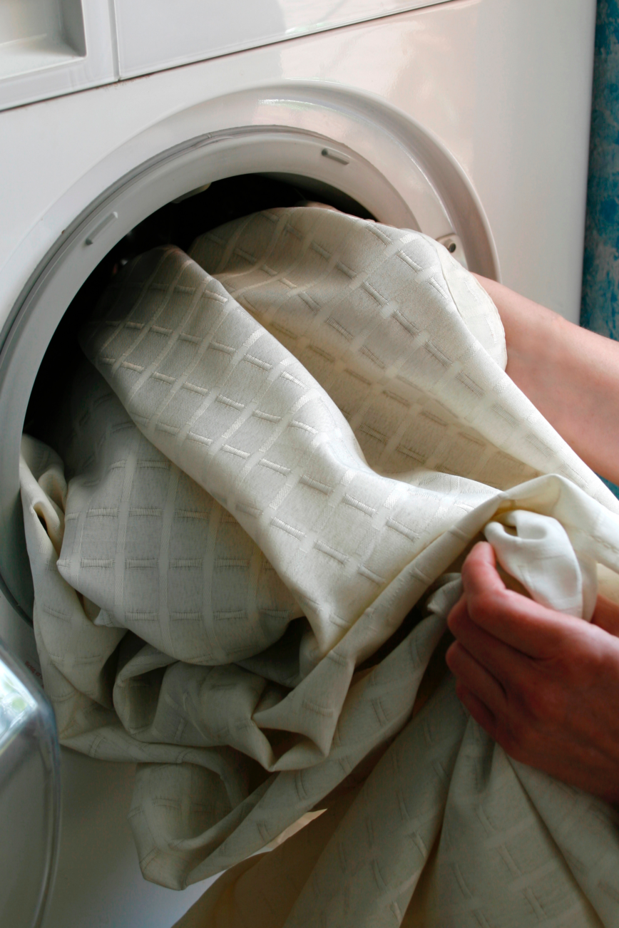 Jemand legt eine helle Gardine in die Waschmaschine. Mithilfe von Gebissreiniger wird sie wieder richtig sauber.
